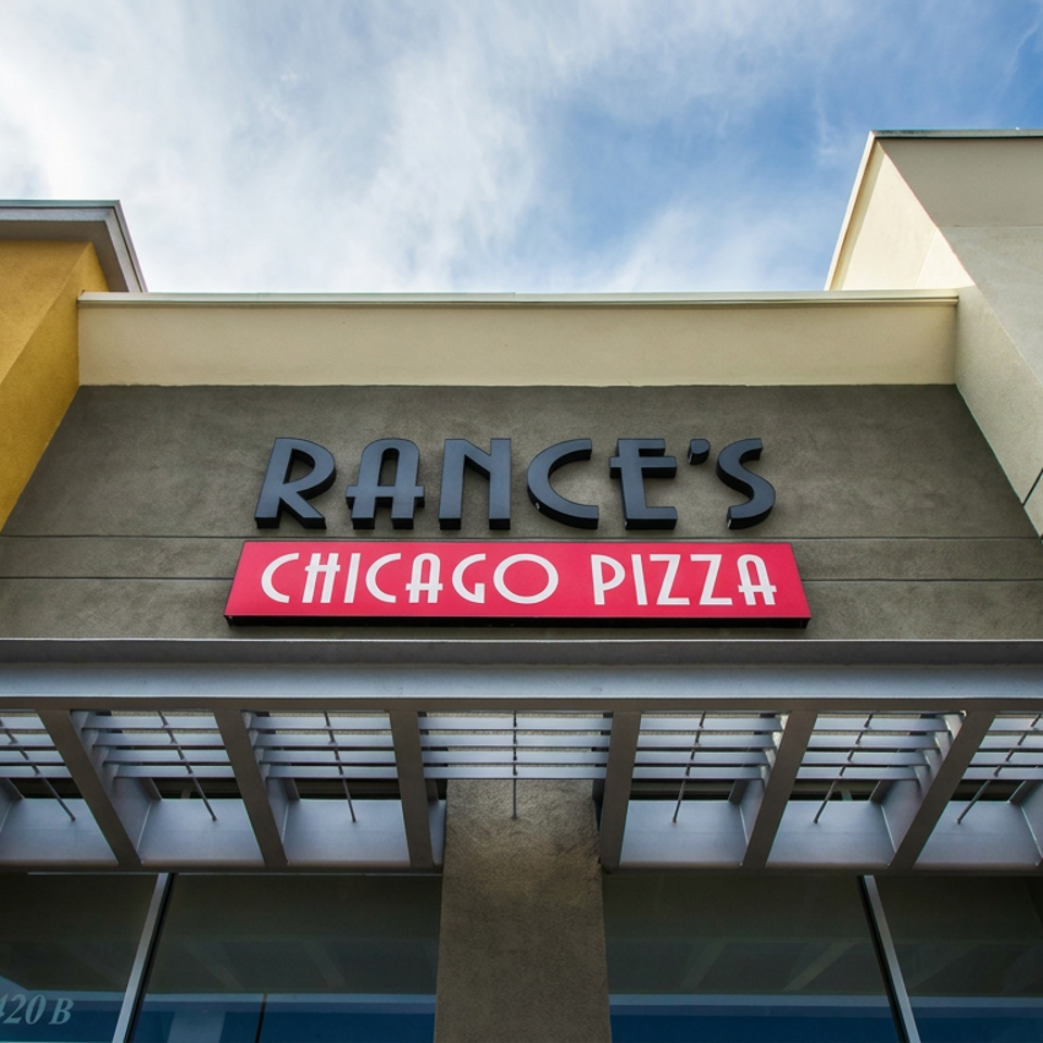 Exterior facade of Rance’s Chicago Pizza restaurant with prominent signage beneath a glass-and-metal awning.